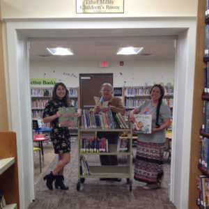Three womensmiling standing with Library cart in a library